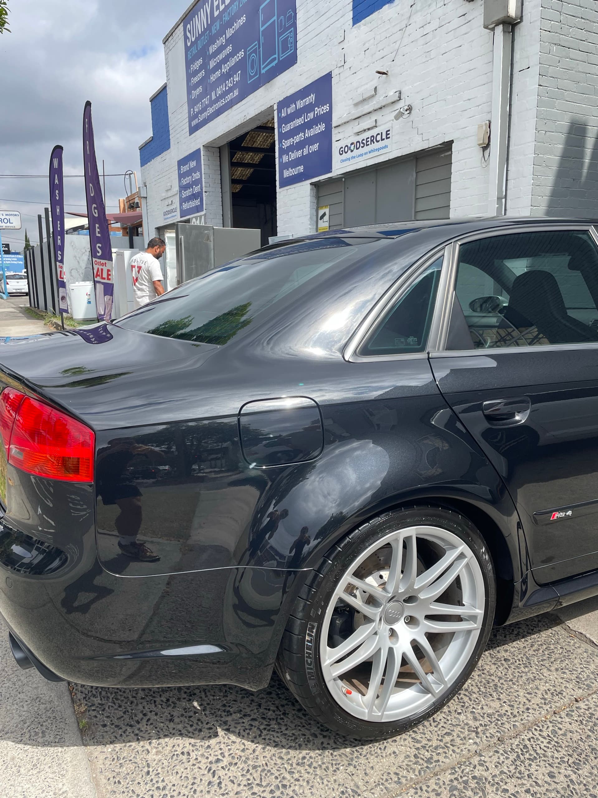 Rear quarter of a black Audi RS4 sedan with a silver alloy wheel and reflections in its glossy paint