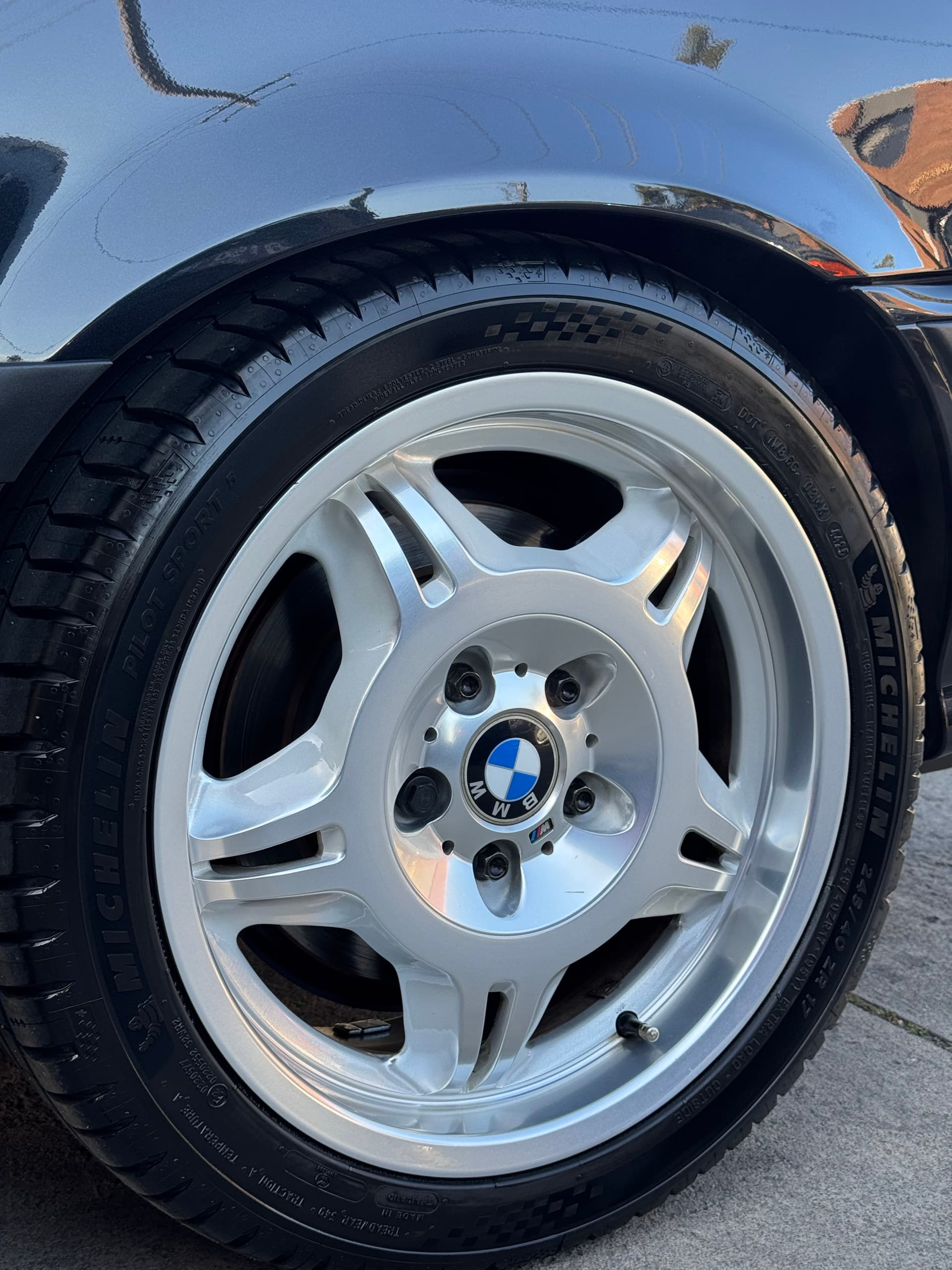 Close-up of a polished silver BMW M alloy wheel on a black E36 M3