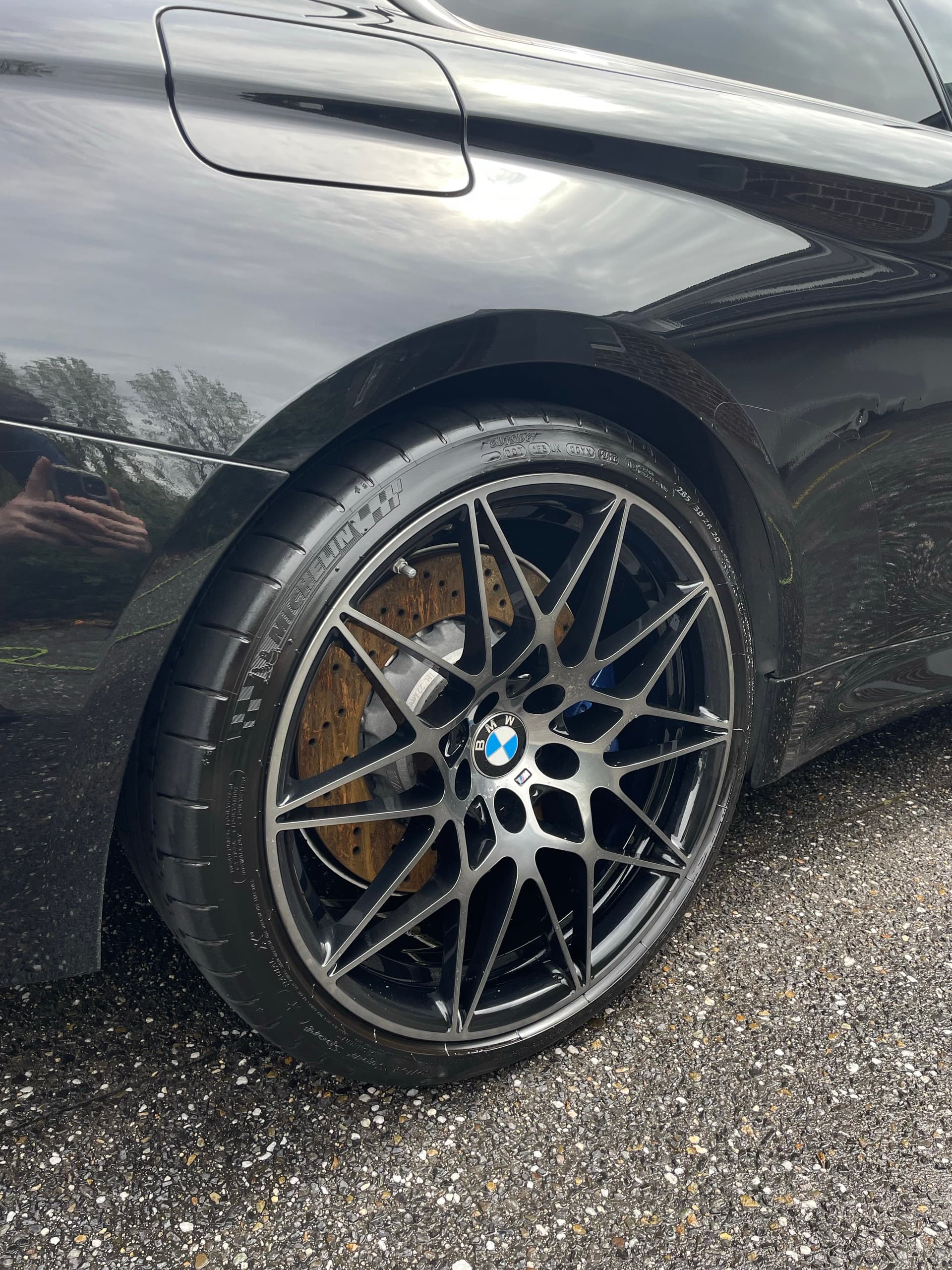 Black alloy wheel with gold brake calipers on a glossy black BMW M4