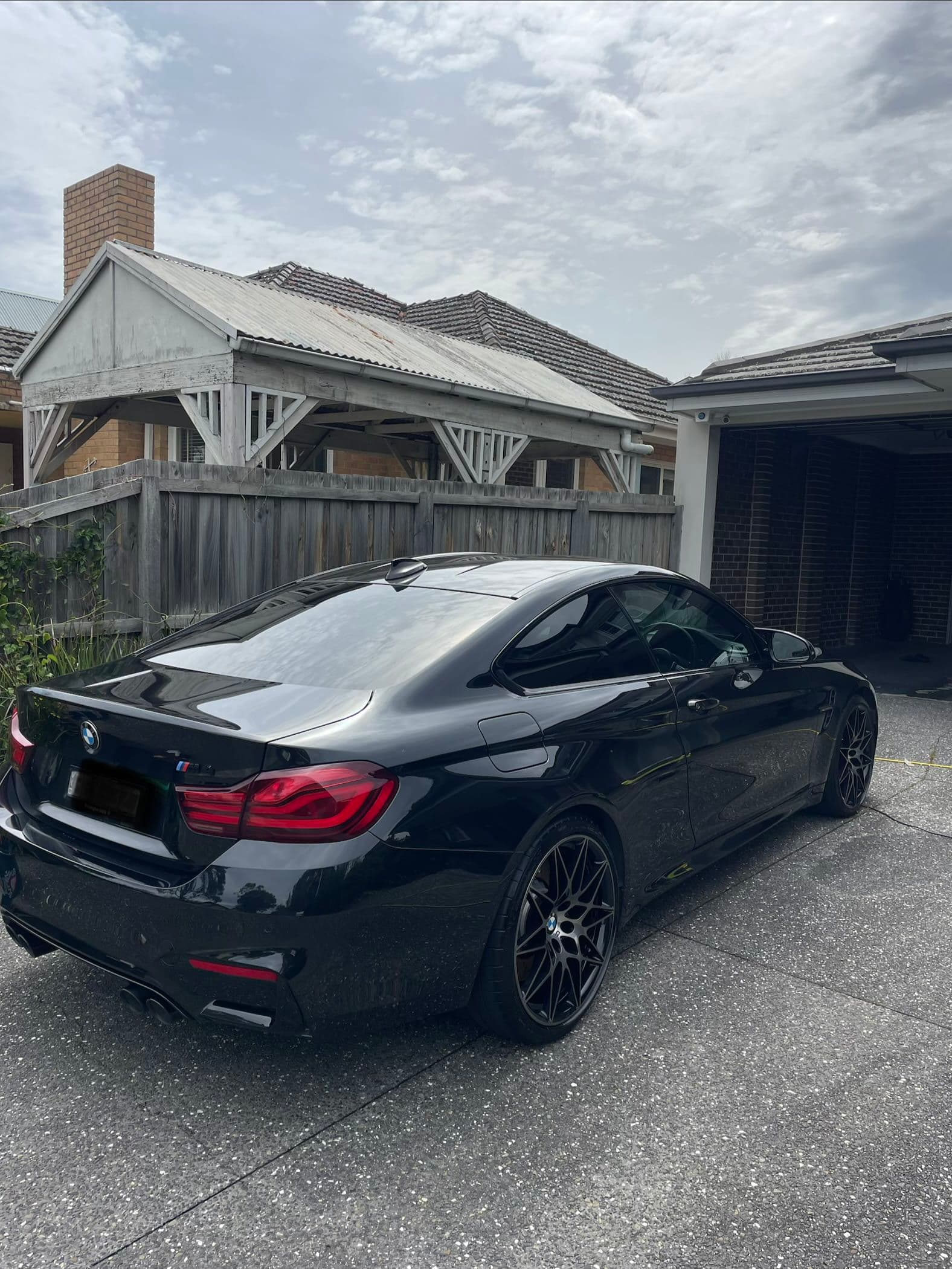 Rear three-quarter view of a black BMW M4 coupe parked in a driveway
