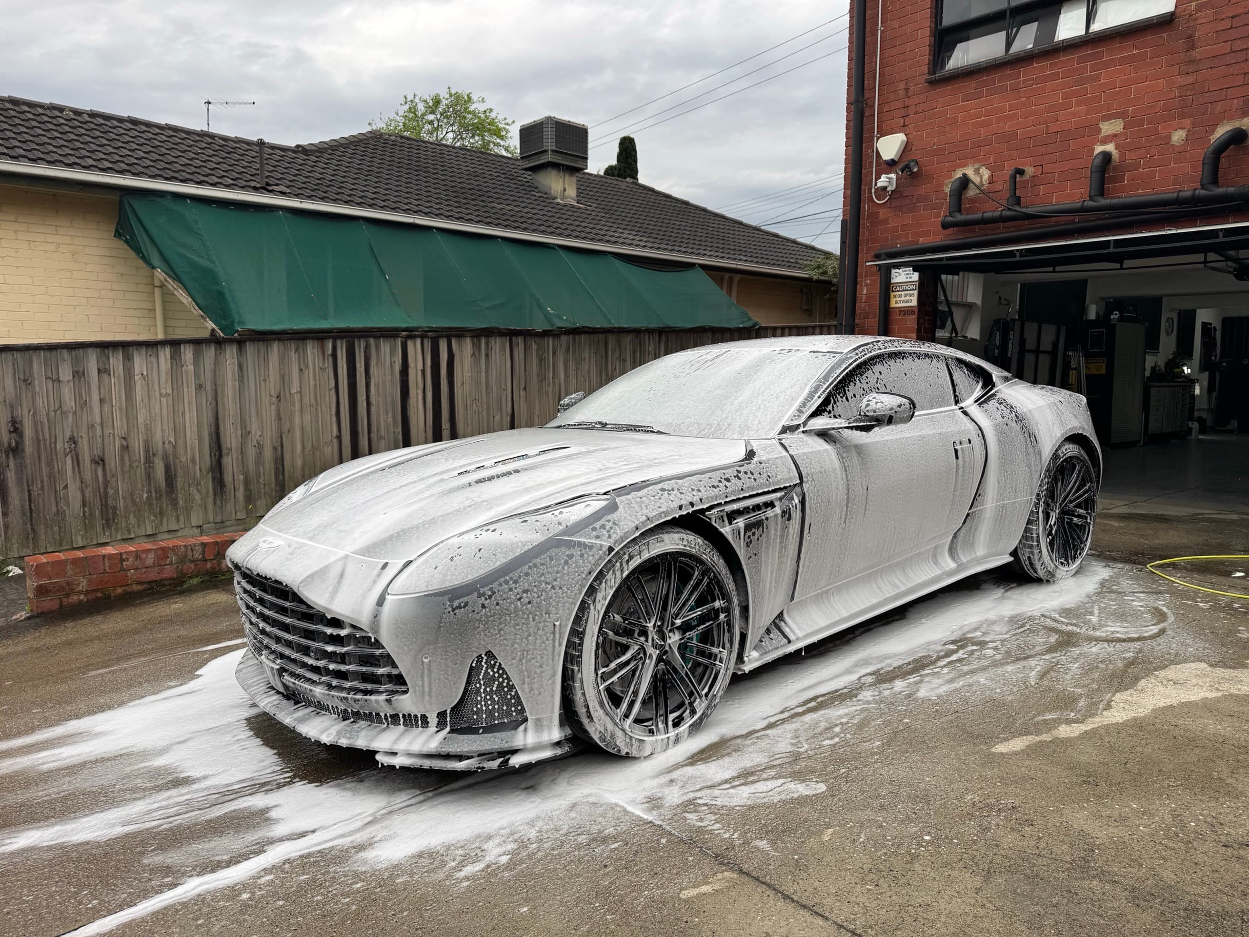Grey Aston Martin DB12 covered in snow foam on a concrete driveway