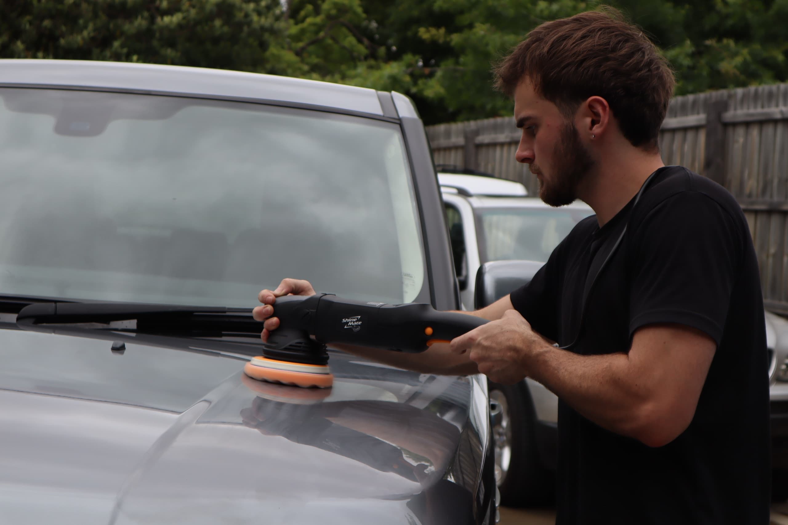 Detailer using a dual-action machine polisher on the bonnet of a grey vehicle
