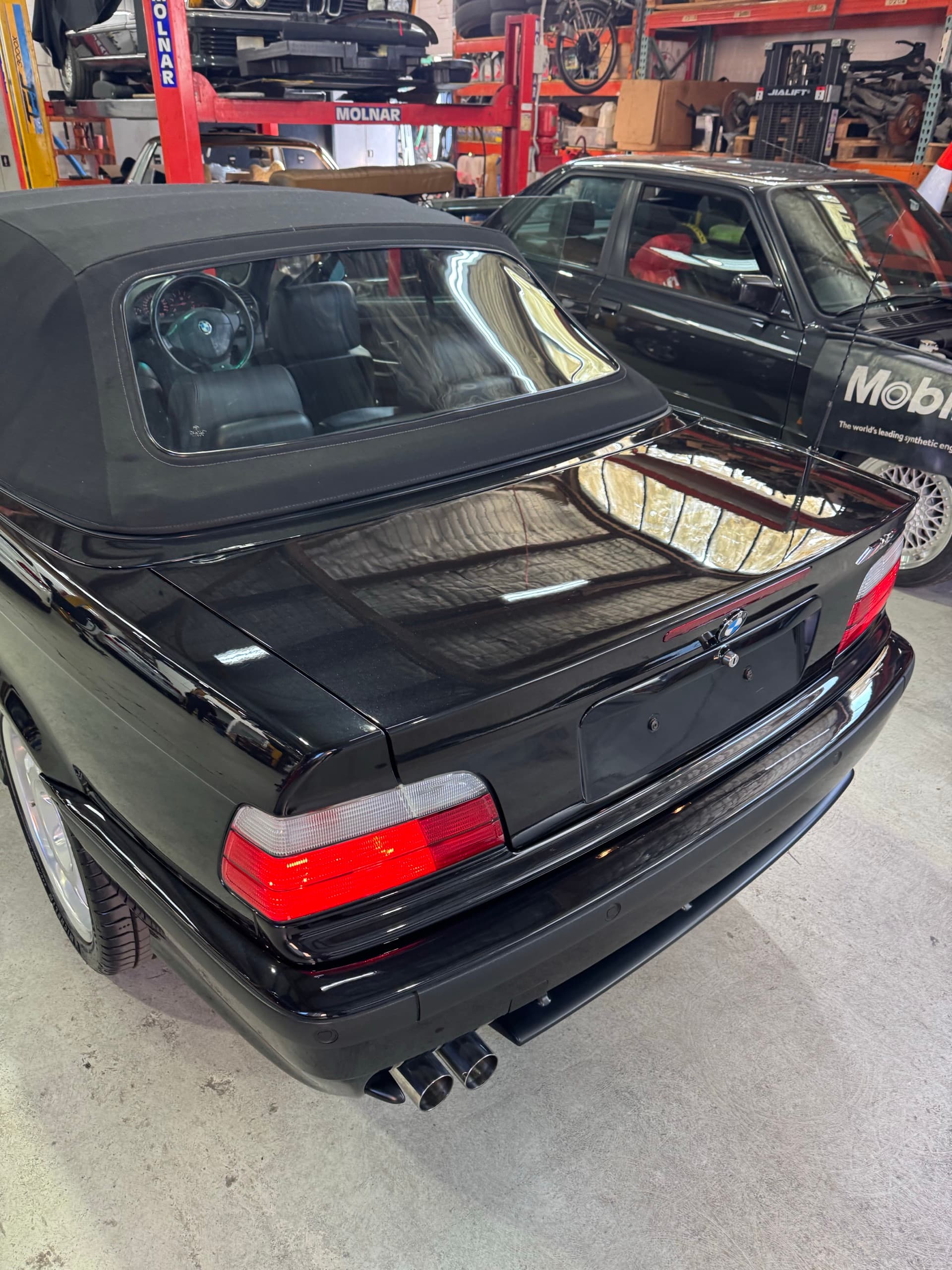 Rear of a black BMW E36 M3 convertible with workshop lights reflected in the glossy boot lid
