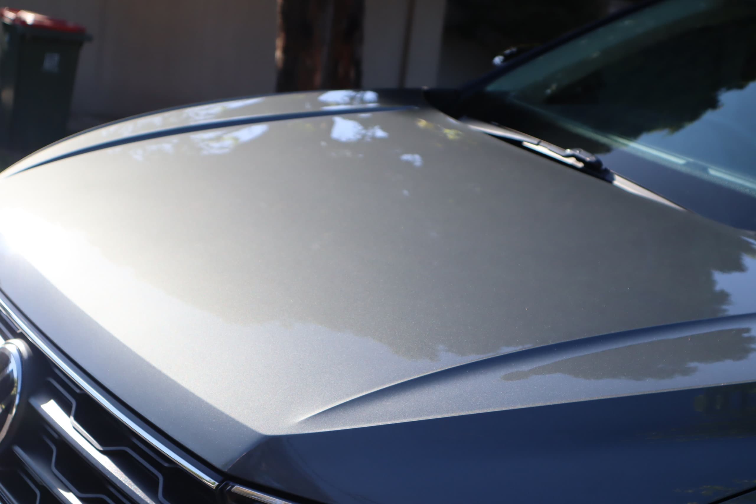 Close-up of a grey Volkswagen bonnet with trees and sky reflected in the glossy paint