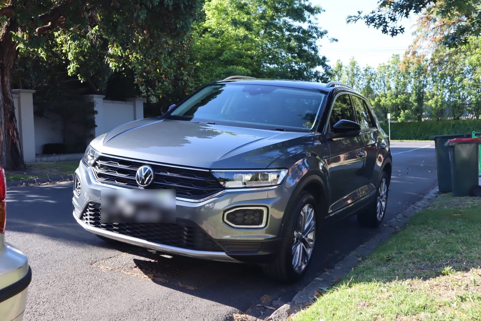 Front three-quarter view of a grey Volkswagen T-Roc parked on a tree-lined street