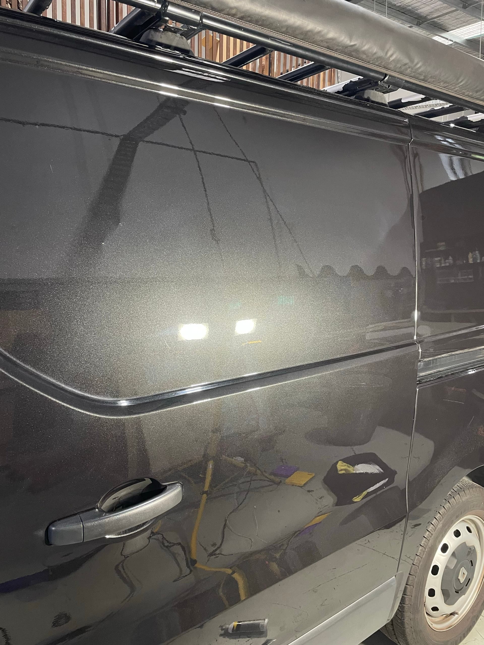 The same dark grey van side panel after paint correction, with a clearer, more even reflection