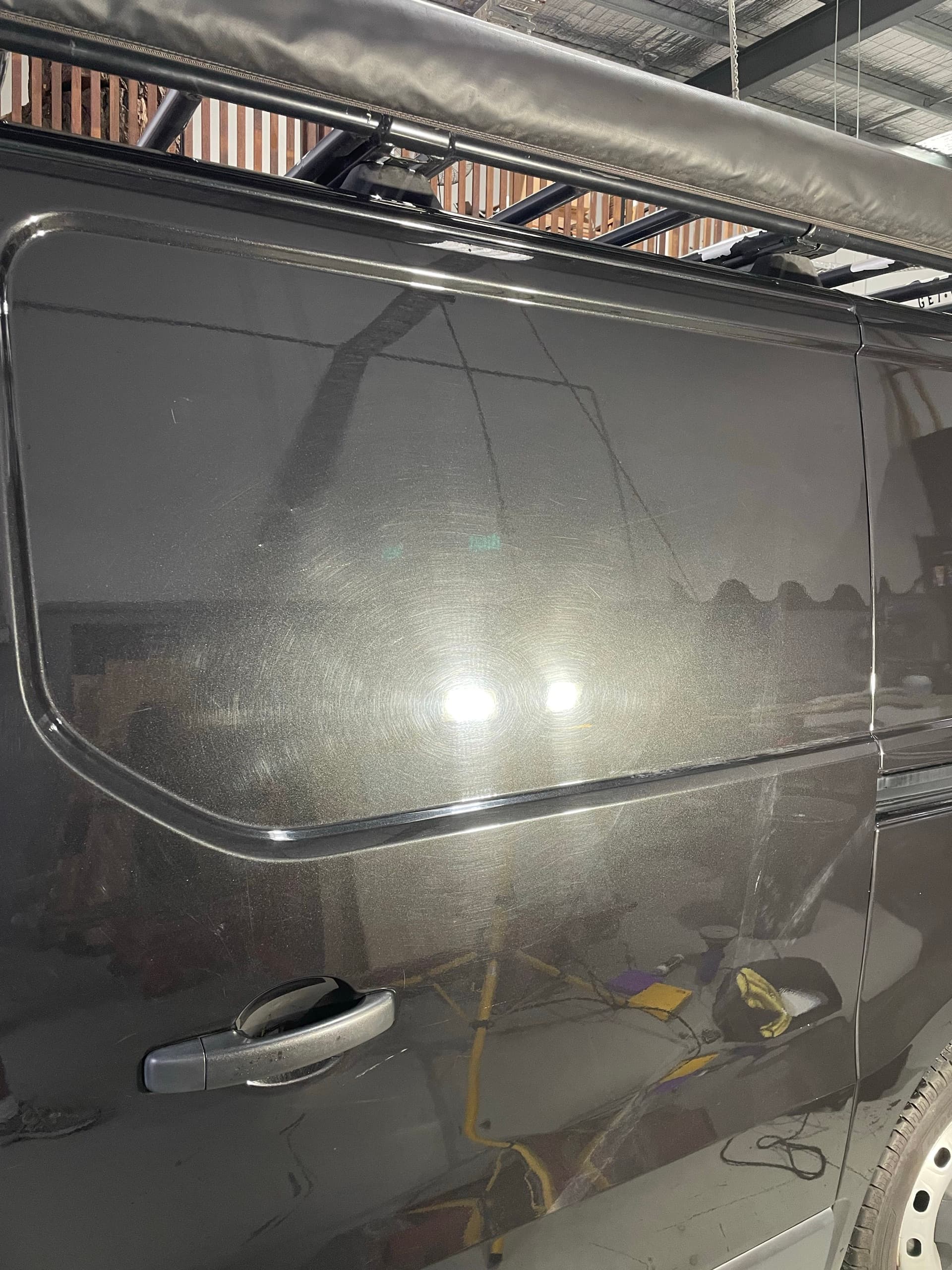 Dark grey van side panel before paint correction, with swirl marks and haze visible around the light reflections