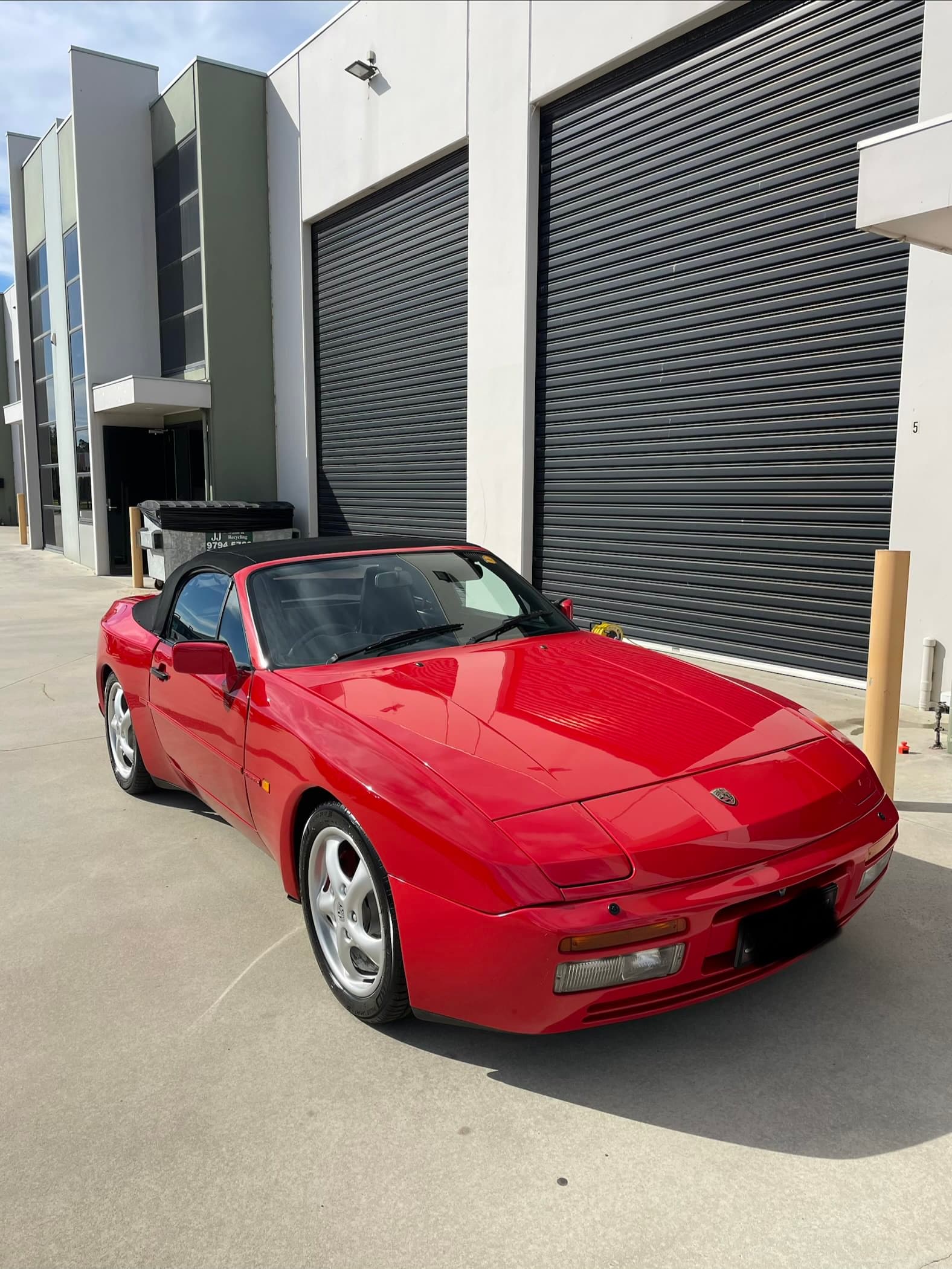 Red Porsche 944 S2 cabriolet parked in front of warehouse roller doors