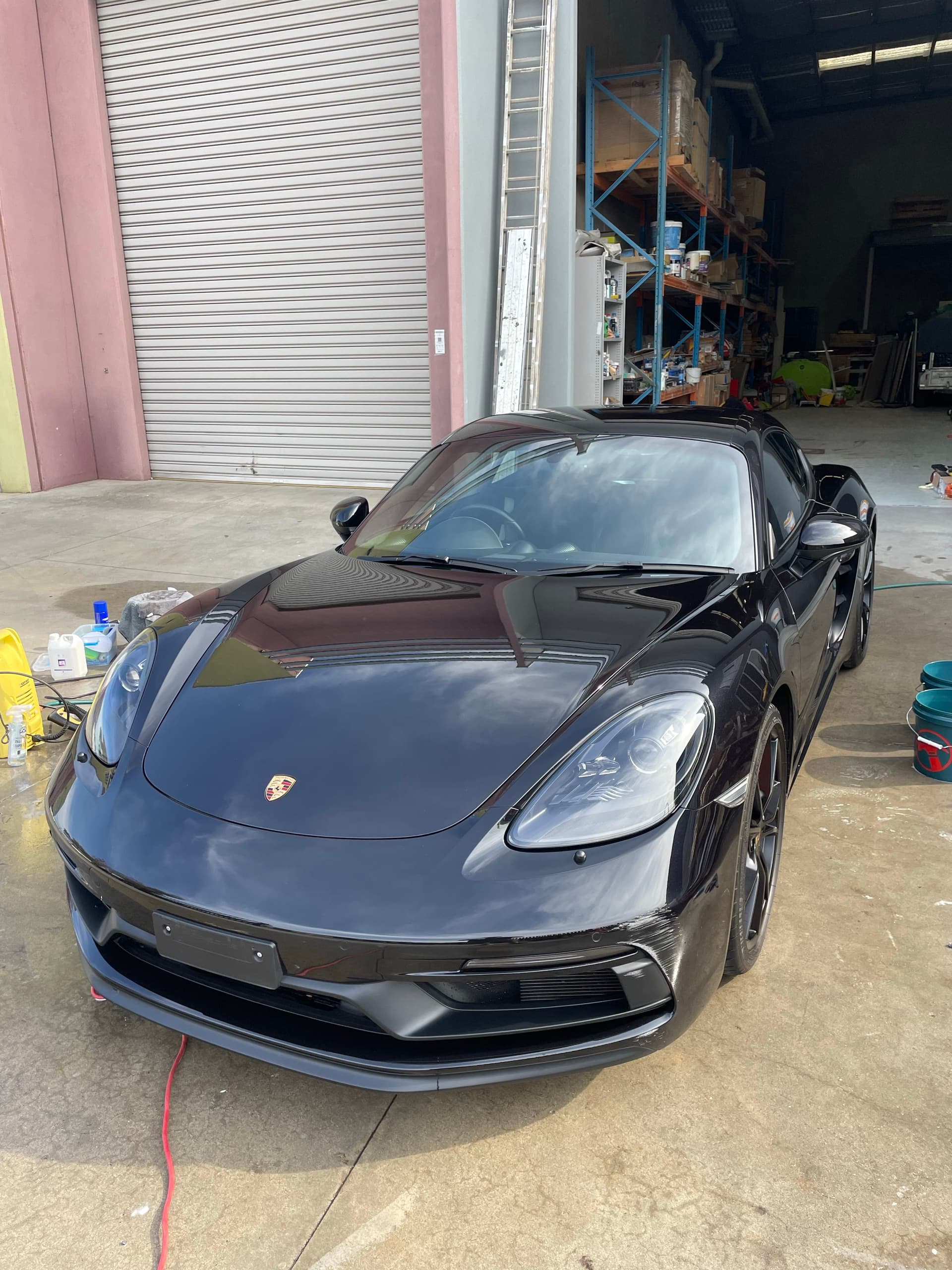 Black Porsche Cayman GTS parked in front of a roller door, with light reflected along its glossy paint