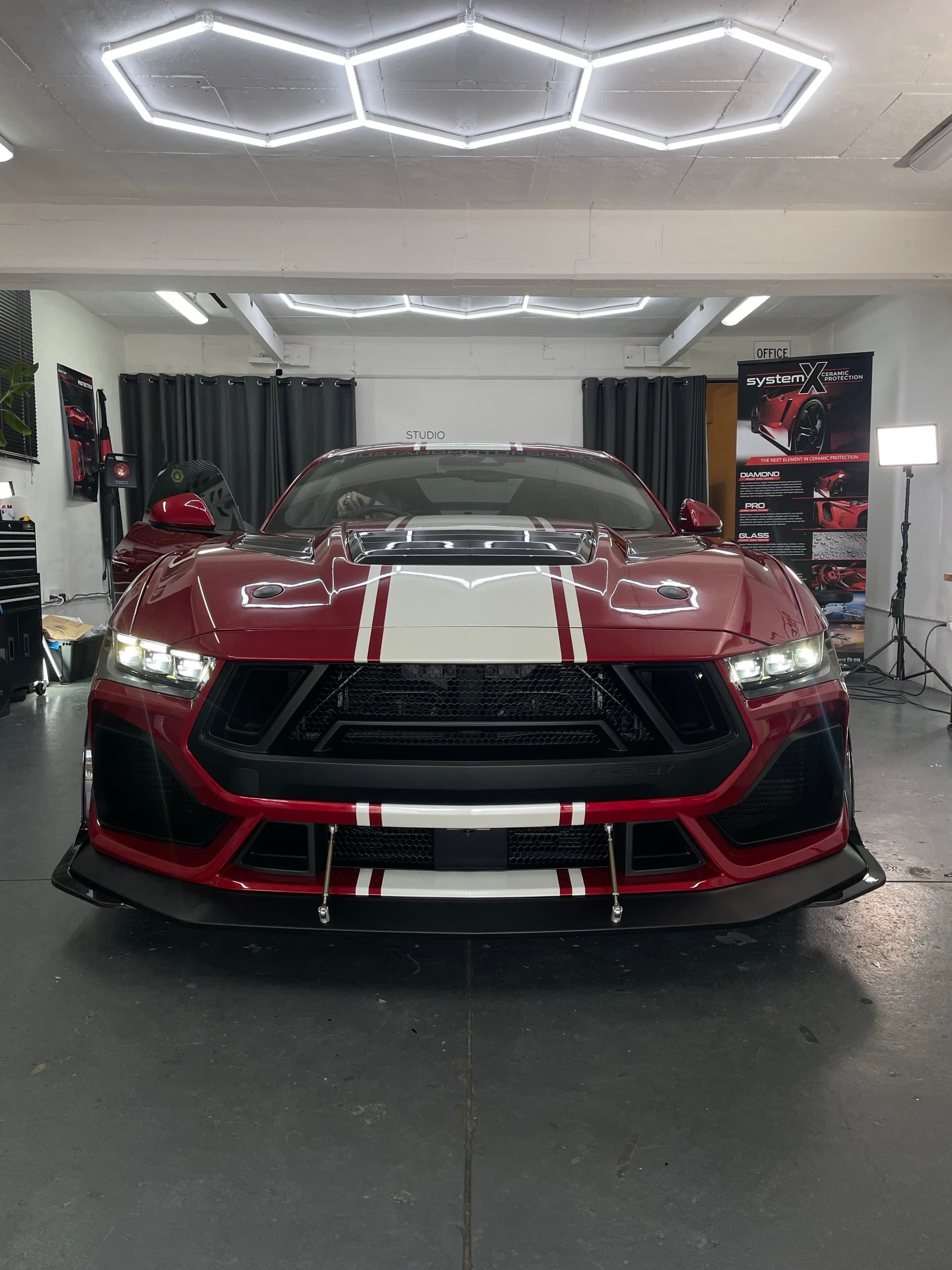Front of a red Ford Mustang Super Snake with white stripes under hexagonal studio lights