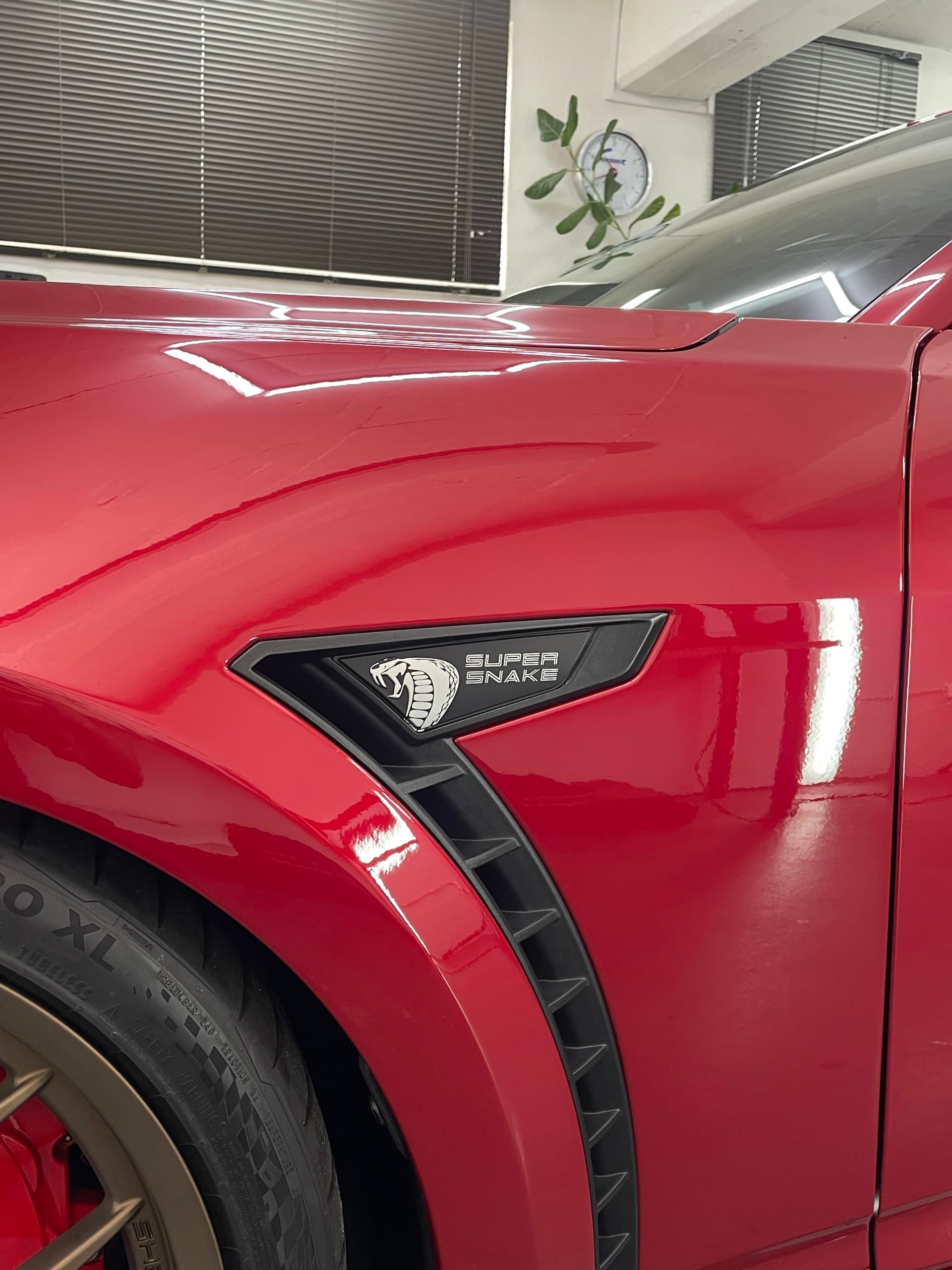 Front guard of a red Ford Mustang Super Snake, with its vent badge and lights reflected in the glossy paint