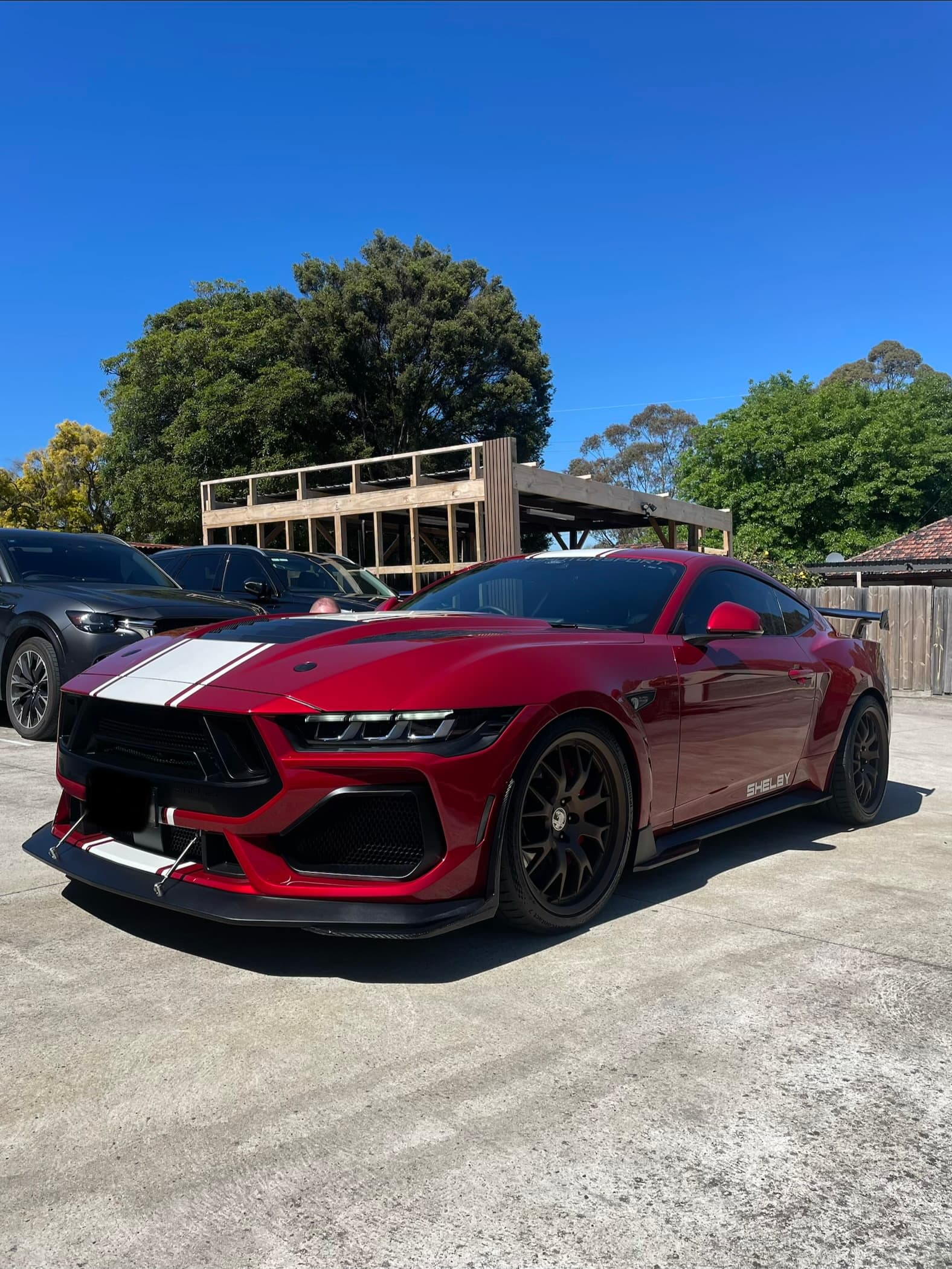Front three-quarter view of a red Ford Mustang Super Snake with white stripes under a blue sky