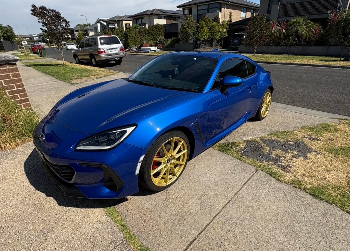 Blue Subaru BRZ with gold alloy wheels parked on a suburban driveway